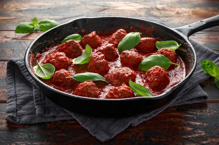 Homemade Meatballs in iron cast with sweet and hot tomato sauce, basil. On wooden table
